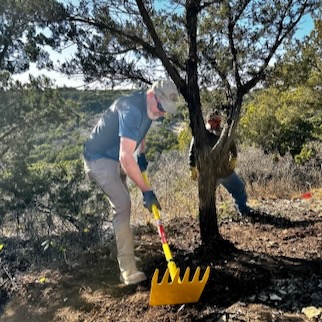 A student uses a McLeod or rakehoe to level and remove rocks from a trail path. 