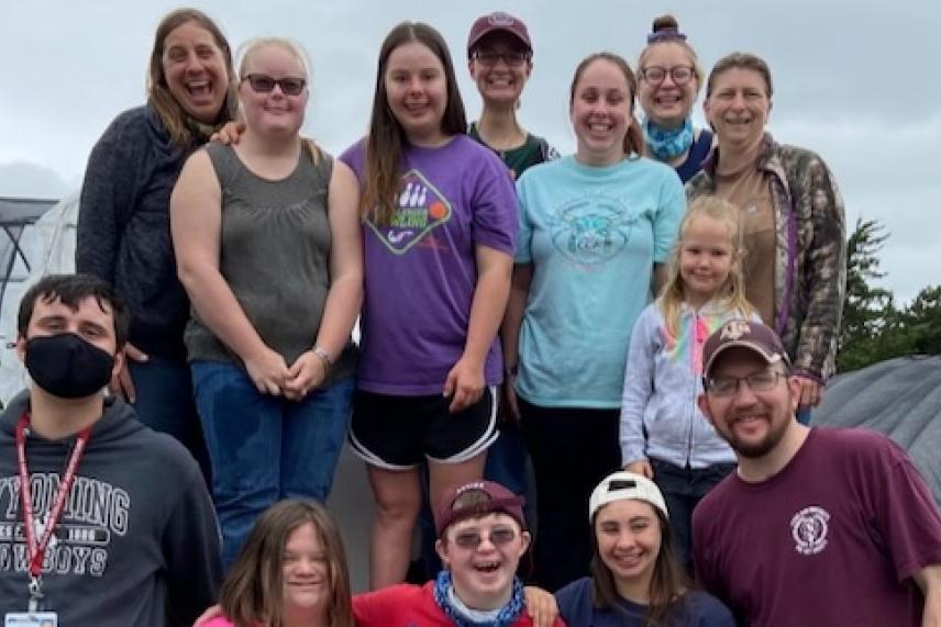 Group of people smiling in an outdoor setting, some wearing colorful shirts and caps.