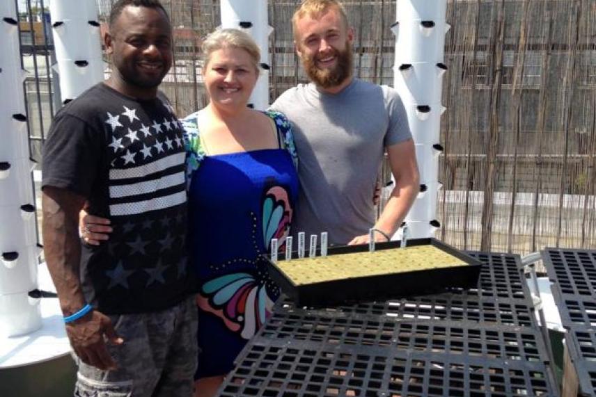Three people smiling on a rooftop with gardening tables and planters.