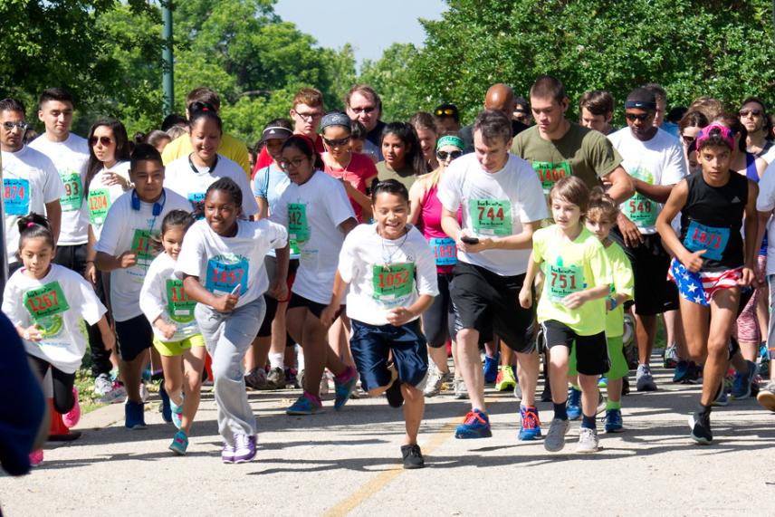 Kids and adults running in a group, wearing race bibs and colorful shirts.