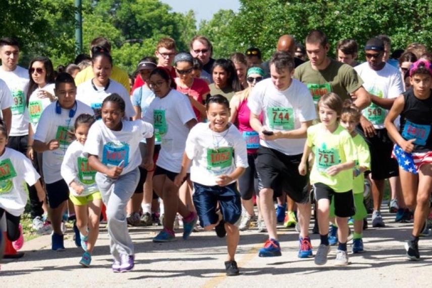 Children and adults joyfully running together in a park race.