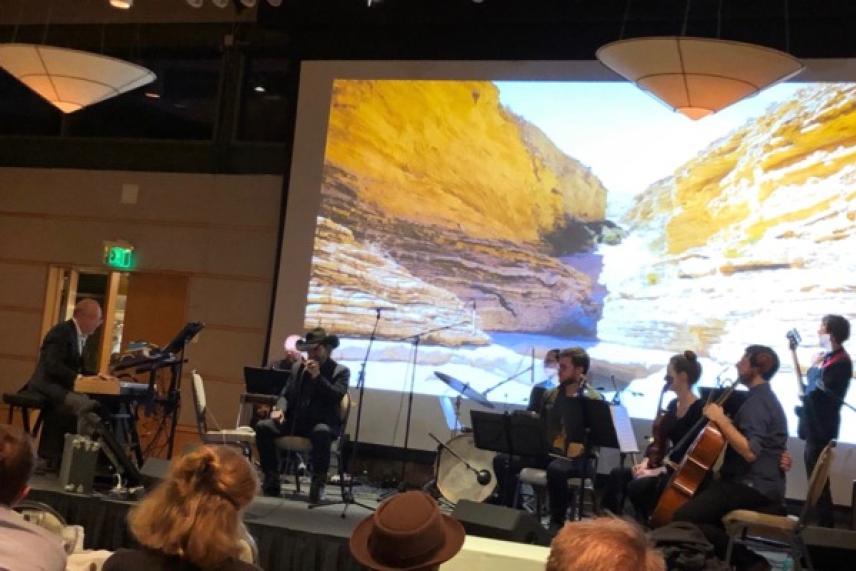 Band playing on stage with desert canyon image on a large screen behind them.