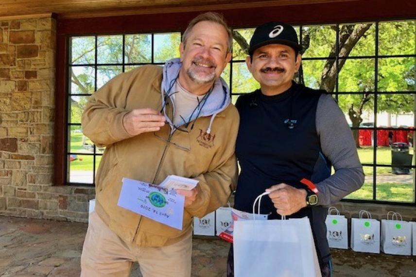 Two smiling men standing under a porch, holding prizes.