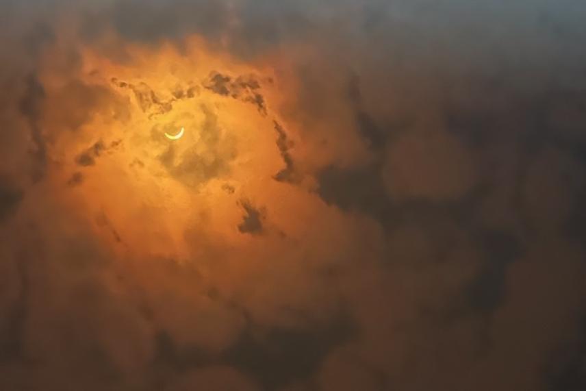 Crescent moon glowing through thick orange clouds.