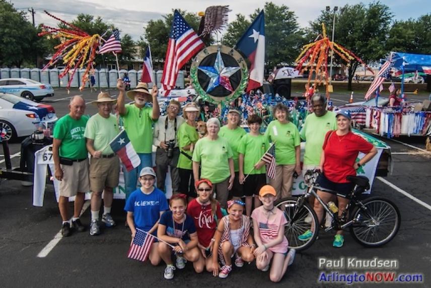 Group posing with flags near decorated float with star and USA theme.