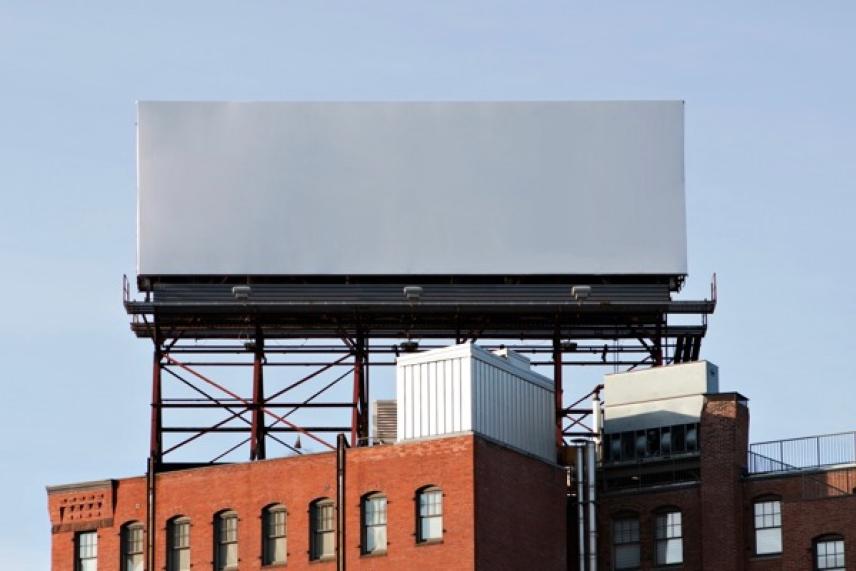 Blank billboard atop a red brick building against blue sky.