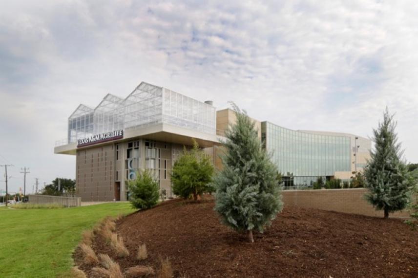 Modern building with glass façade, surrounded by trees and a landscaped garden.
