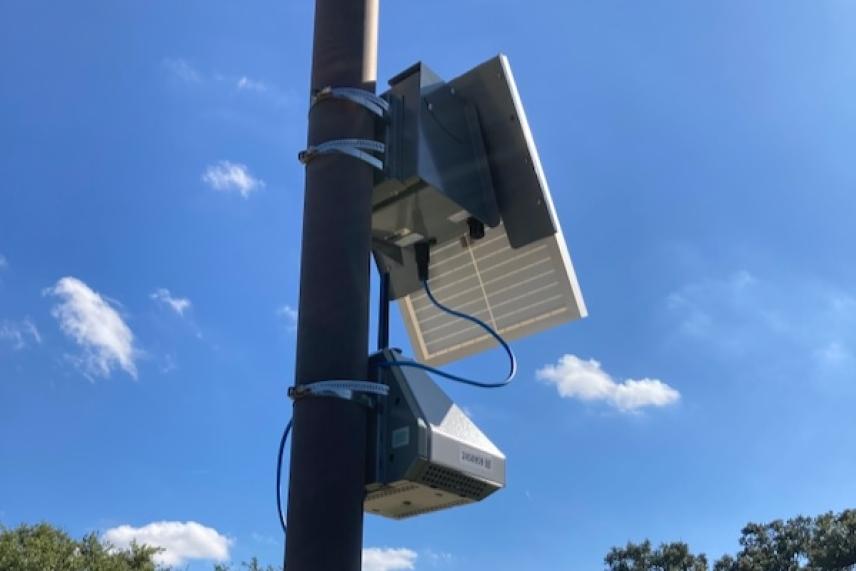 Solar panel and air monitoring devices mounted on a pole under a clear blue sky.