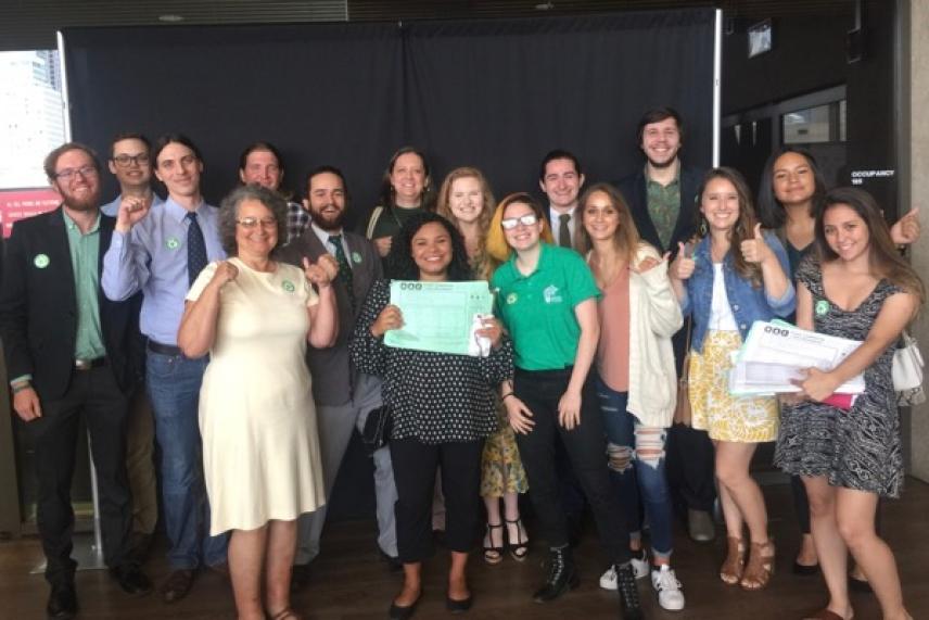 Group of people smiling, standing indoors, holding certificates and papers.