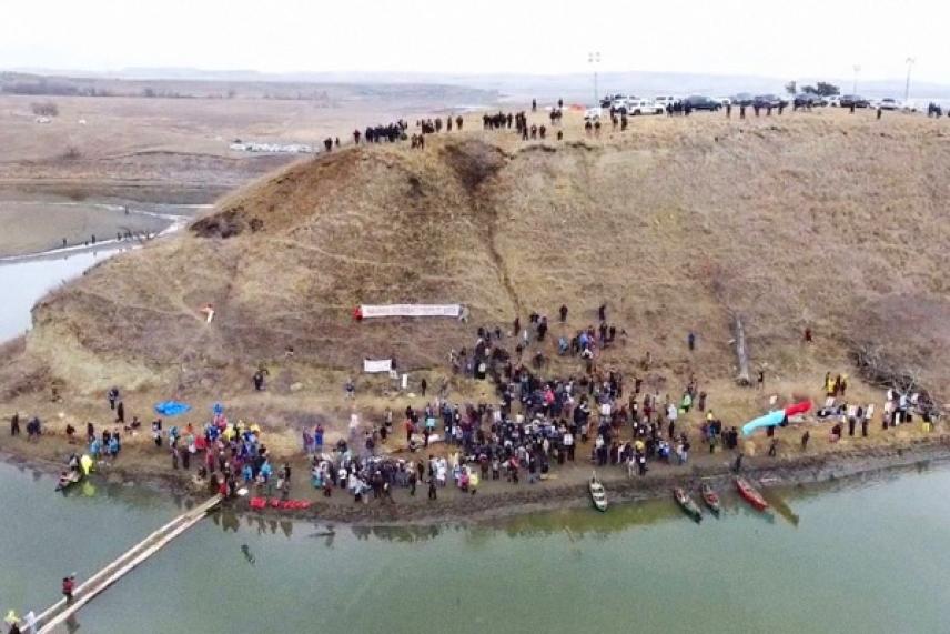 Crowd gathered on a hill by a river, aerial view.