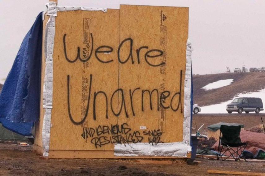 Protest sign on plywood reads "We are Unarmed." Snowy landscape in background.