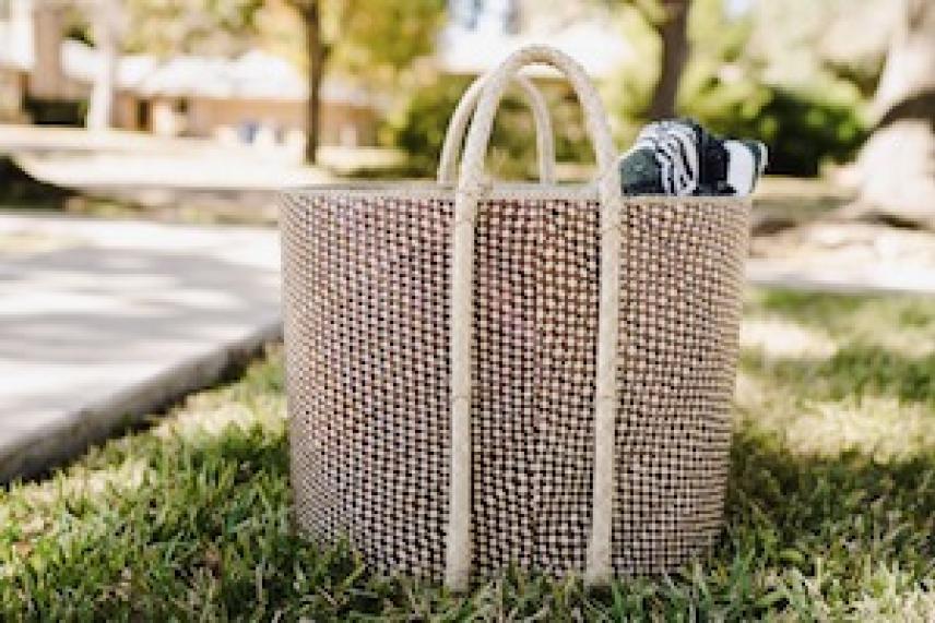 Woven basket with handles on grass, containing rolled-up towels.