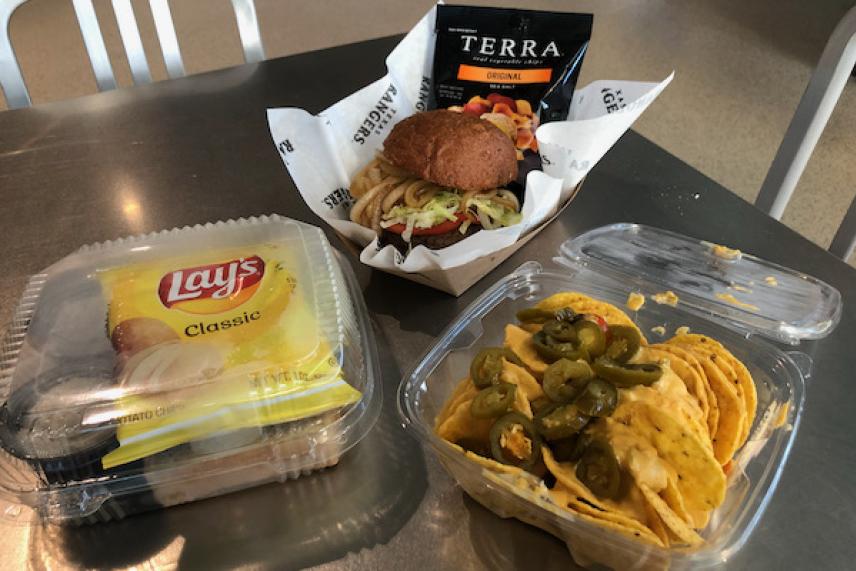 Burger, chips, and nachos with jalapeños on a table.