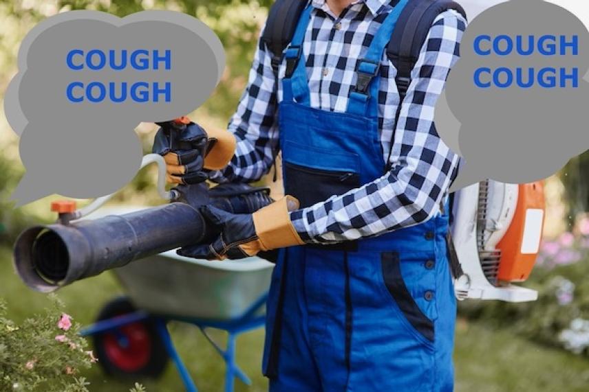 Worker in blue overalls using a leaf blower outdoors.