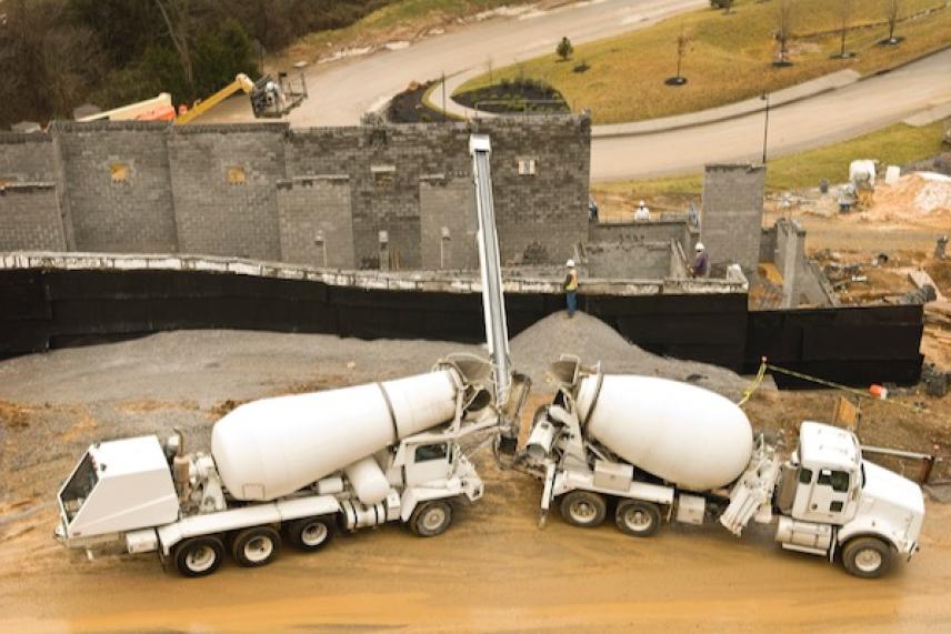 Concrete trucks at a construction site near a partially built gray wall.