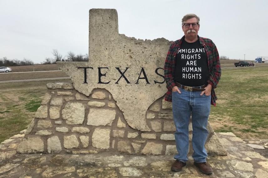 Man standing next to a stone Texas sign in a grassy area.