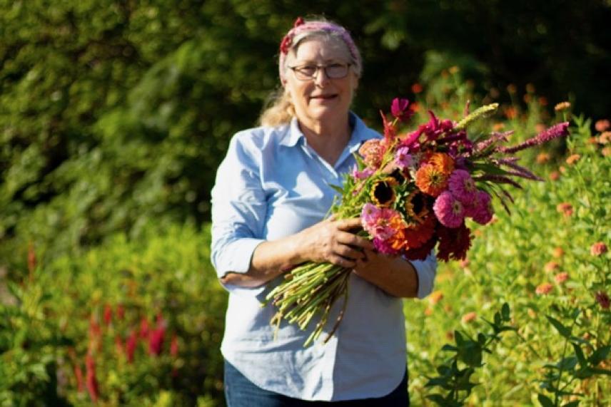 Woman smiling, holding a colorful bouquet in a sunny garden.