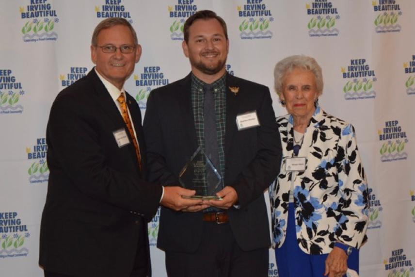 Three people smiling, holding an award, standing against a logoed backdrop.
