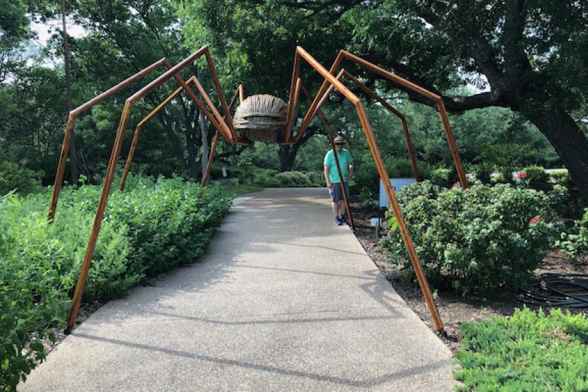 Giant spider sculpture over a garden pathway, surrounded by greenery.
