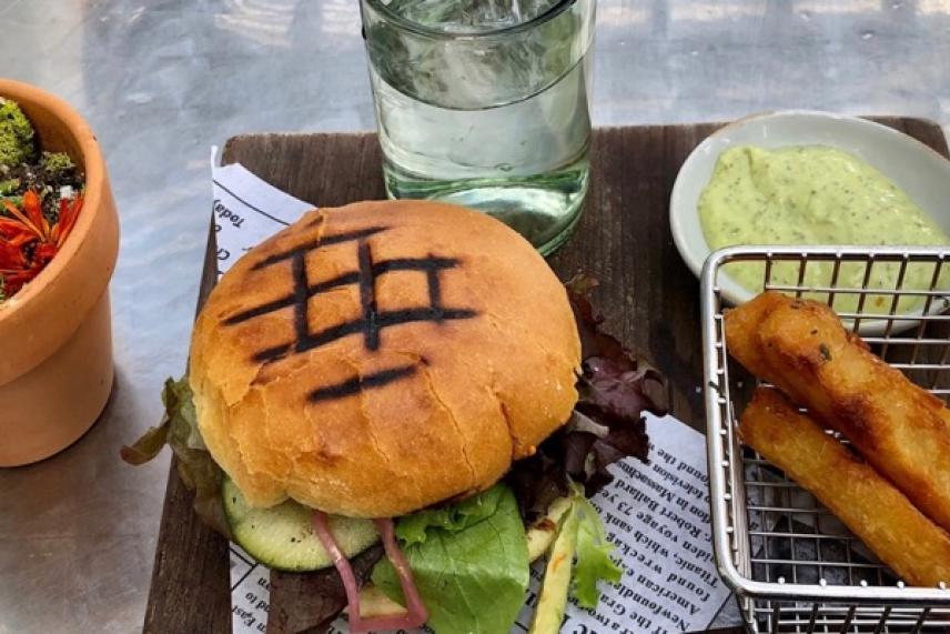 Burger with grilled marks, side of fries, salad, and a glass of water on a table.