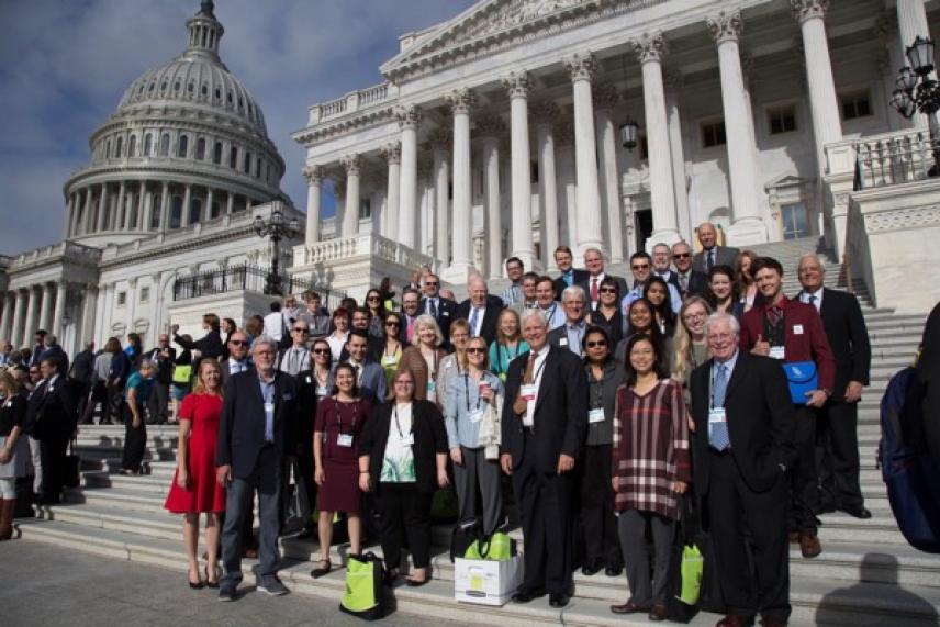 Group of people gathered on Capitol steps, clear day, building in background.
