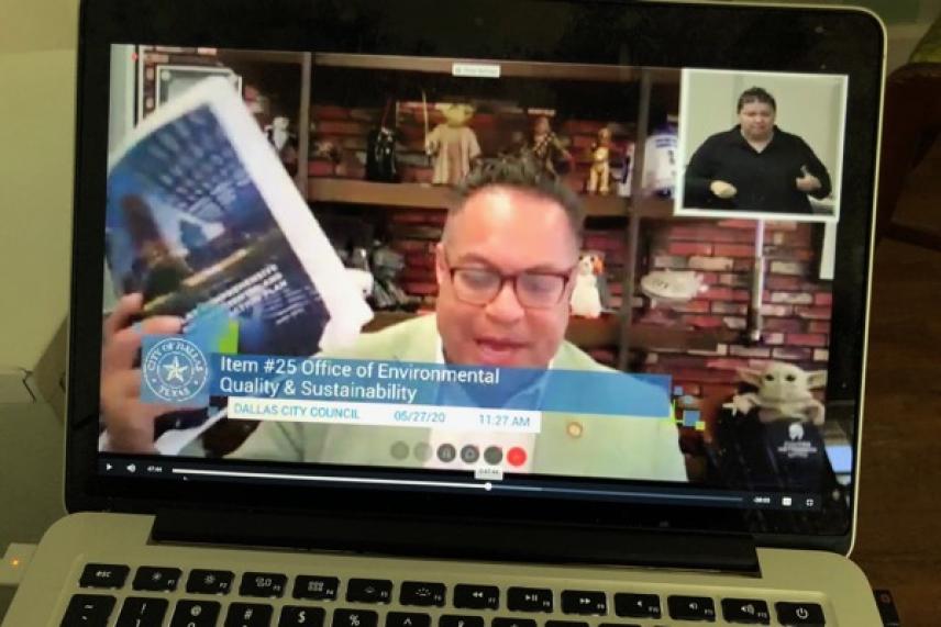 Laptop screen showing a virtual meeting with a man holding a book and a sign language interpreter.