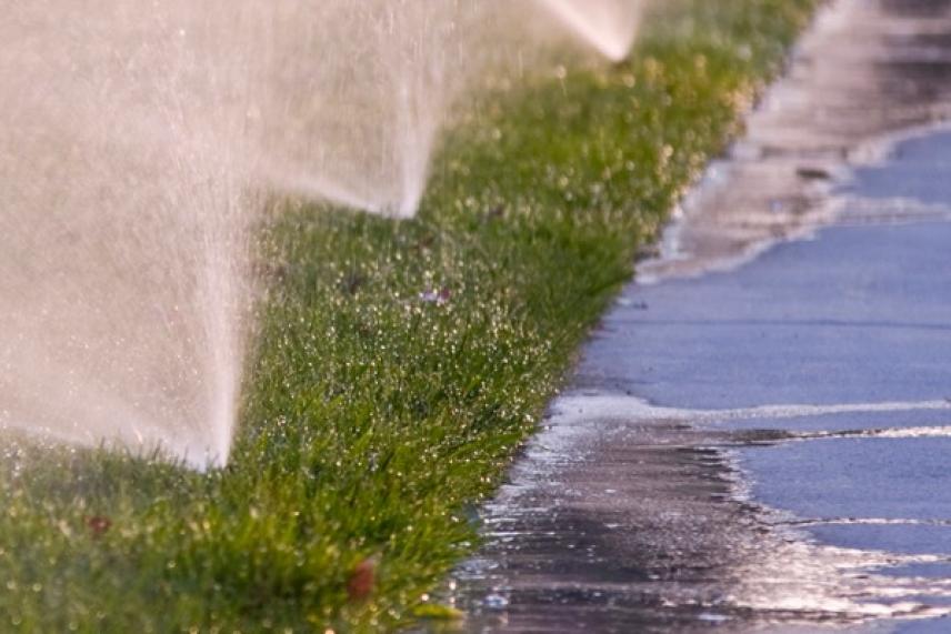 Sprinklers watering green grass near a wet sidewalk.