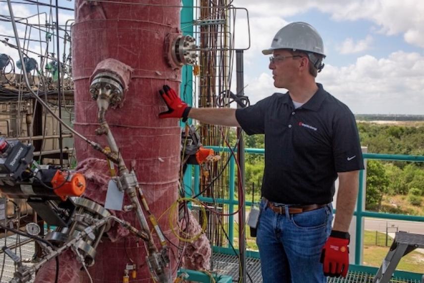 Engineer inspecting industrial pipe outdoors, wearing hard hat and gloves.