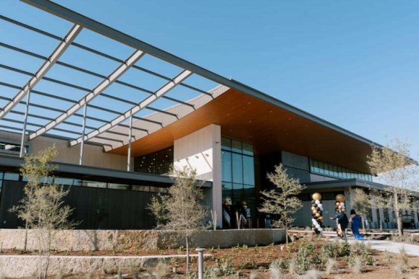 Modern building with glass facade and open metal roof under a clear blue sky.
