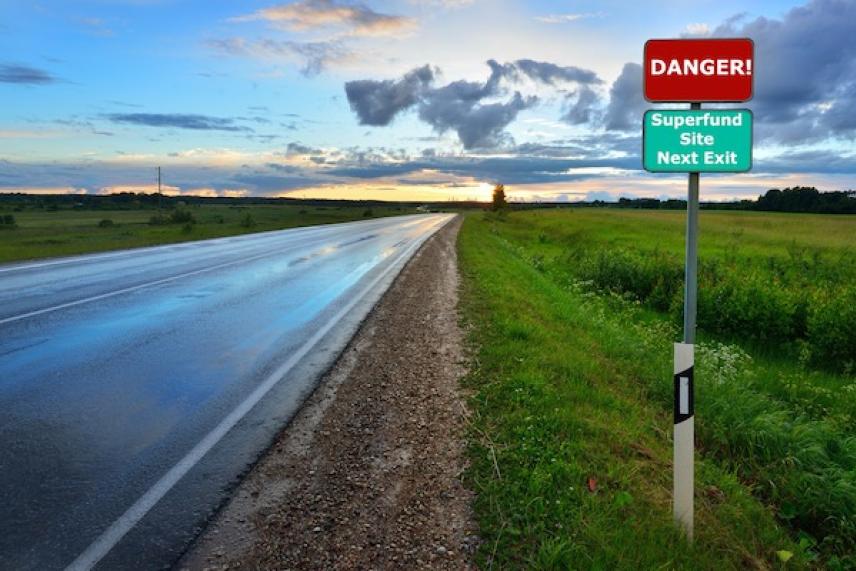 Wet road at sunset with a danger sign on the roadside.