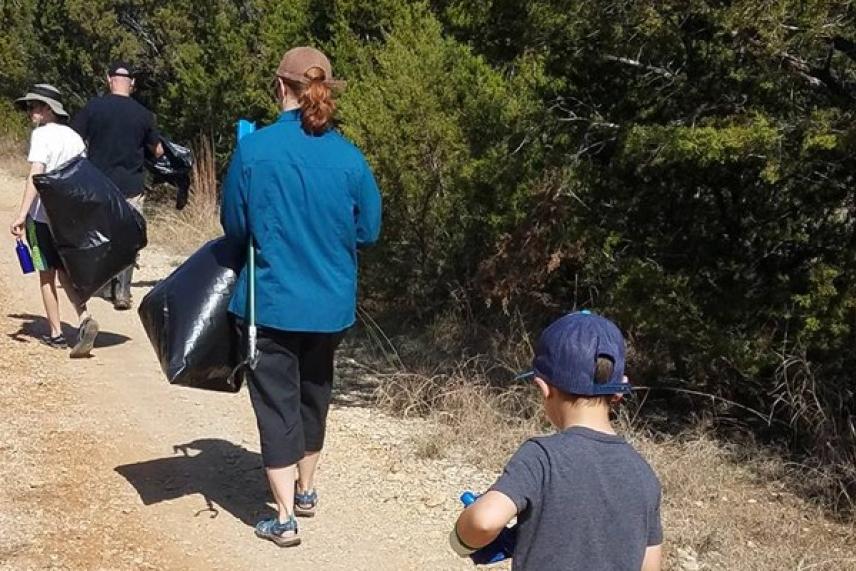 People walking on a trail carrying trash bags, surrounded by trees.