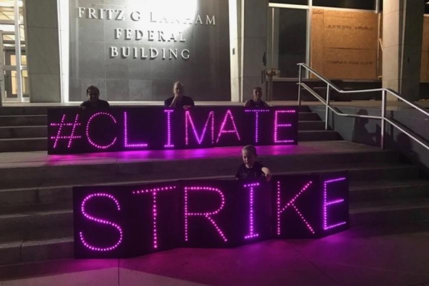 Protesters holding illuminated signs reading "#Climate Strike" on building steps at night.
