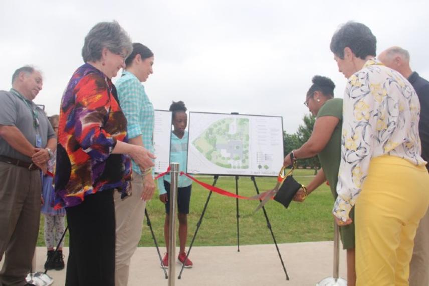 Group of people at a ribbon-cutting ceremony outdoors, with a map on display.