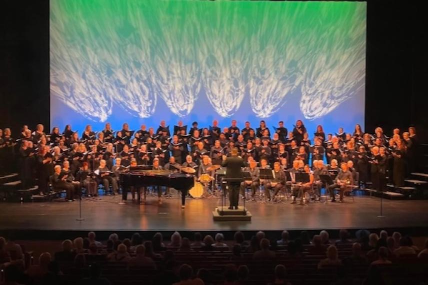 Concert choir performing on a stage with blue and green backdrop lighting.