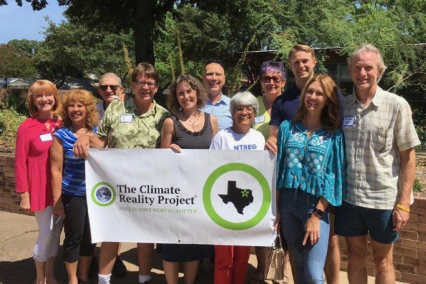 Group of eleven people smiling outdoors, holding a "The Climate Reality Project" banner.