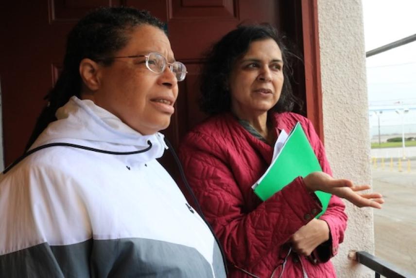 Two women talking outside, one holding green folders.