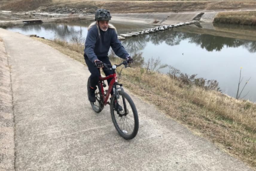 Cyclist riding along a riverside path on a cloudy day.