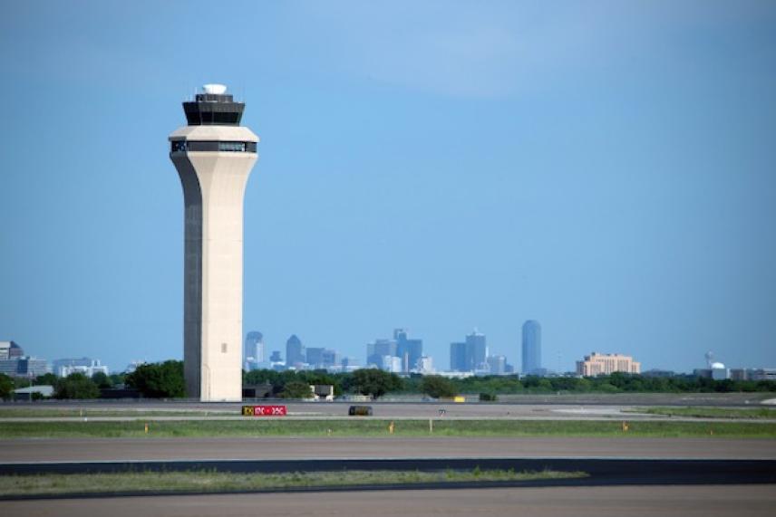 Control tower at airport with city skyline in the background.