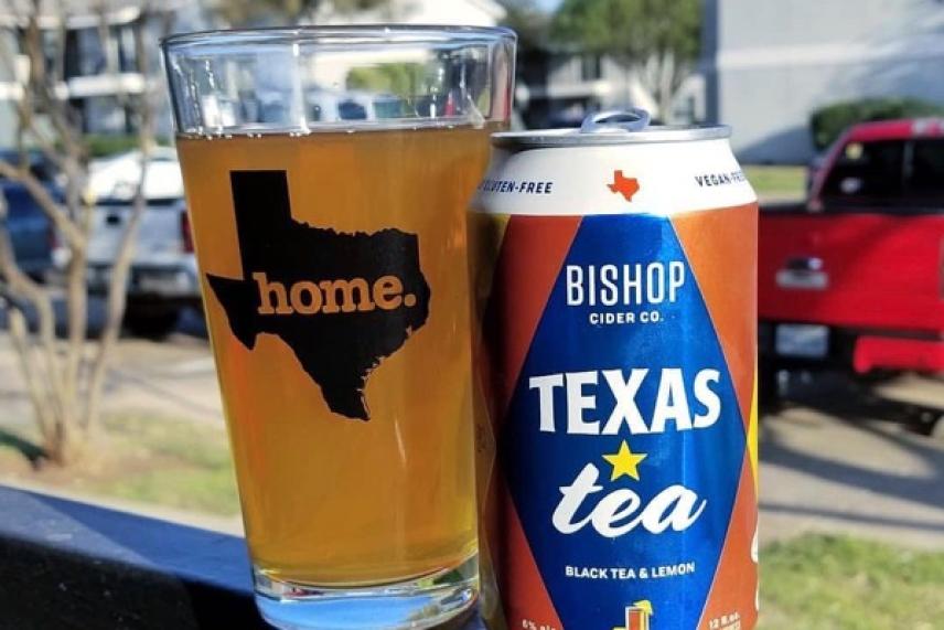 Glass of beer and Texas Tea can on a railing, outdoors.
