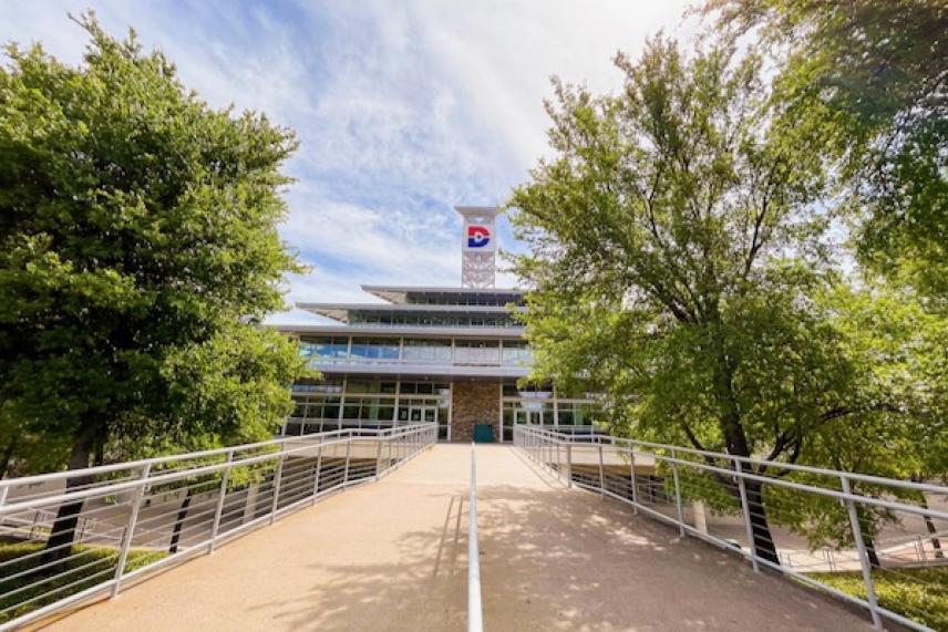 Pathway leading to a modern building among trees under a blue sky.