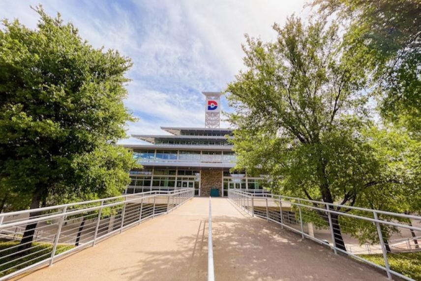 Modern building with a pathway flanked by trees on a sunny day.