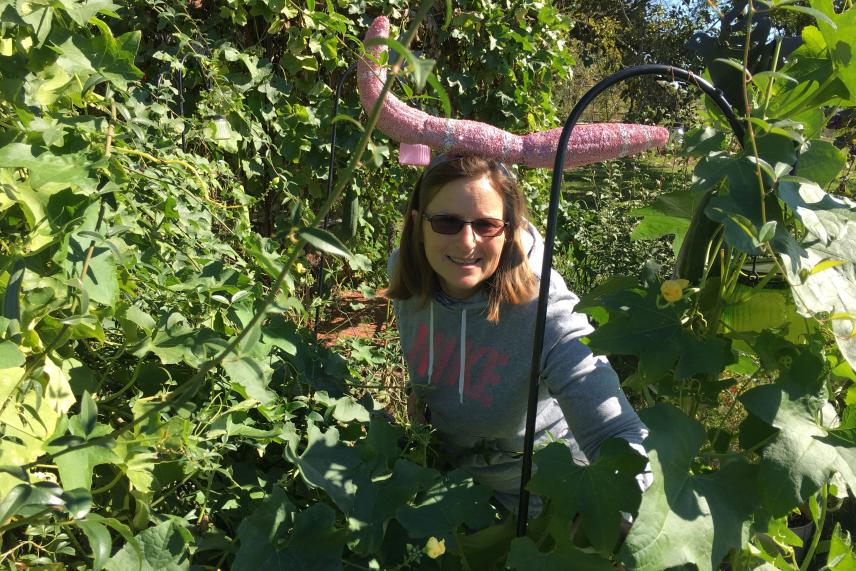 Woman in sunglasses surrounded by green foliage, smiling in a garden.