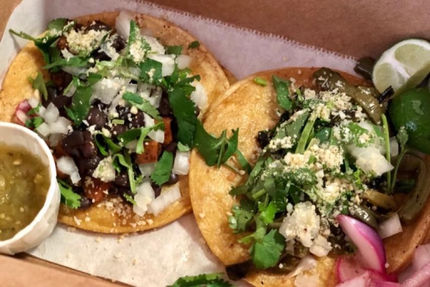 Two tacos with toppings, served with lime and green salsa.