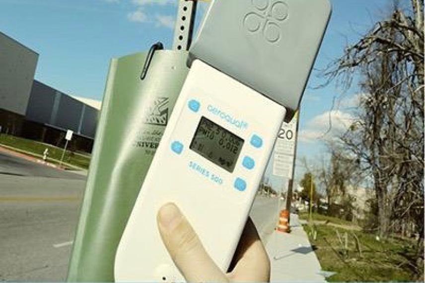 A hand holding a street-level air quality monitor on a sunny day.