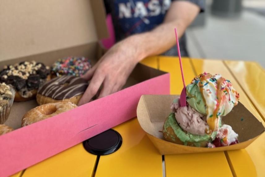 Selection of doughnuts in a box, ice cream scoops next to them on a yellow table.