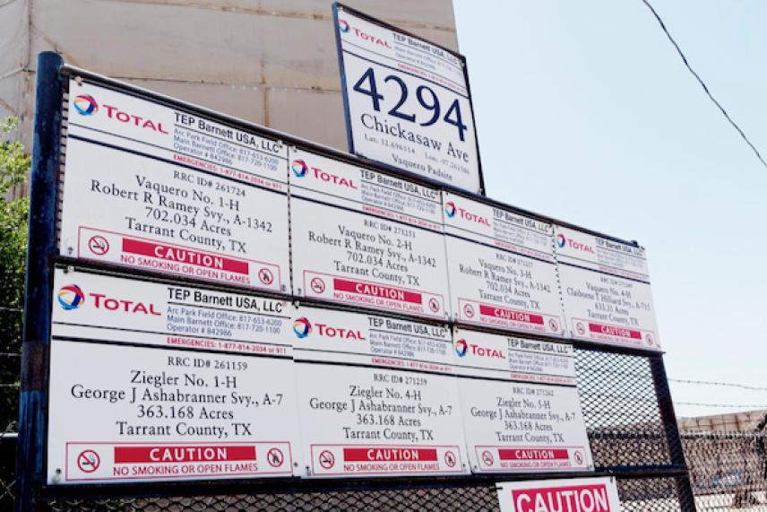 Metal sign displays oil well information and addresses against a clear sky.