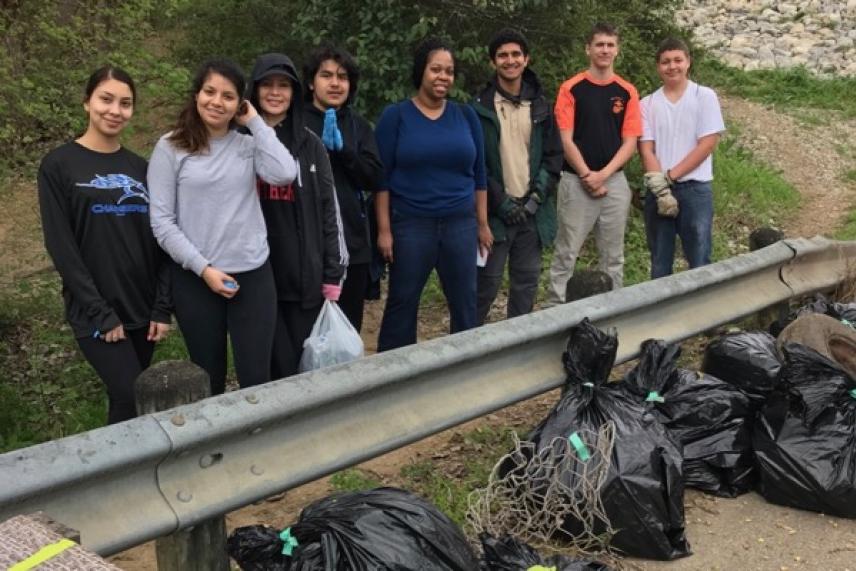 Group of people standing by a roadside with bags of collected trash.