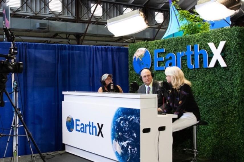 Three people at EarthX booth with cameras and lights set up.