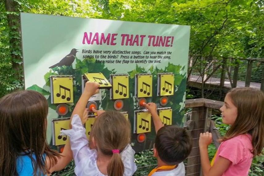 Children pointing at a musical note display in an outdoor setting.