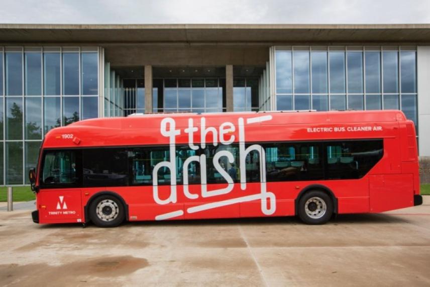 Red electric bus with "the dash" text, parked outside a modern glass building.
